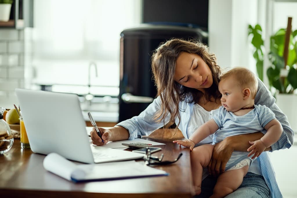 An expecting parent on the phone with insurance paperwork spread across a desk.